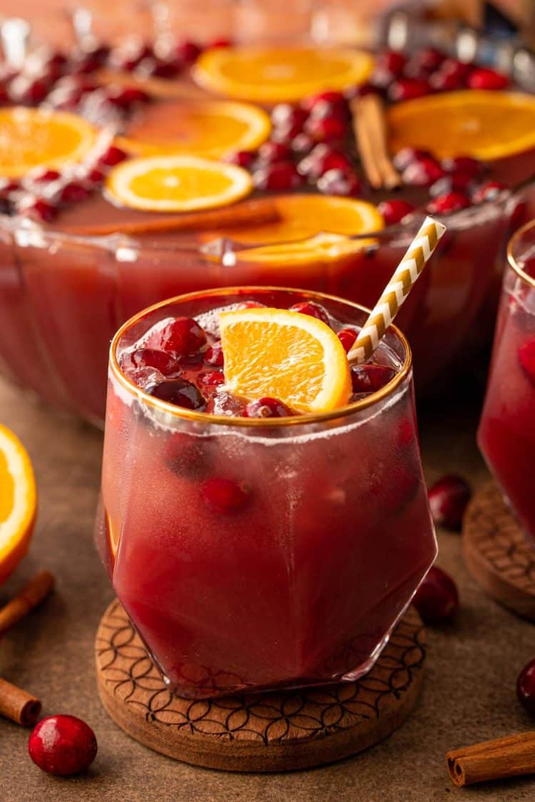 A glass of autumn punch in front of a punch bowl.