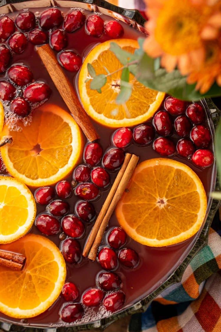 Overhead photo of a bowl of fall punch topped with cranberries, cinnamon, and oranges.