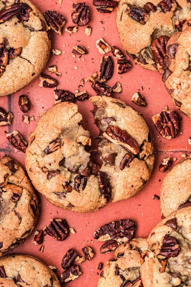 Cookies made with brown butter, pecans, and chocolate on a rust colored surface.
