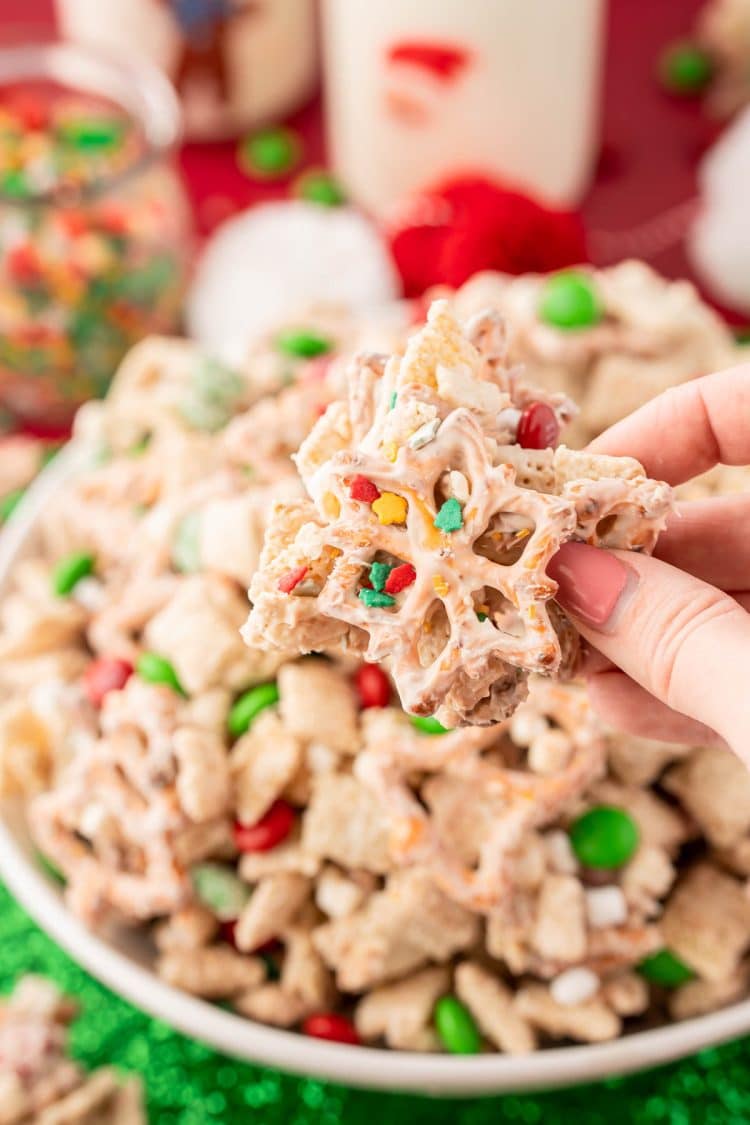 A woman's hand holding a clump of Christmas Chex Snack Mix to the camera.