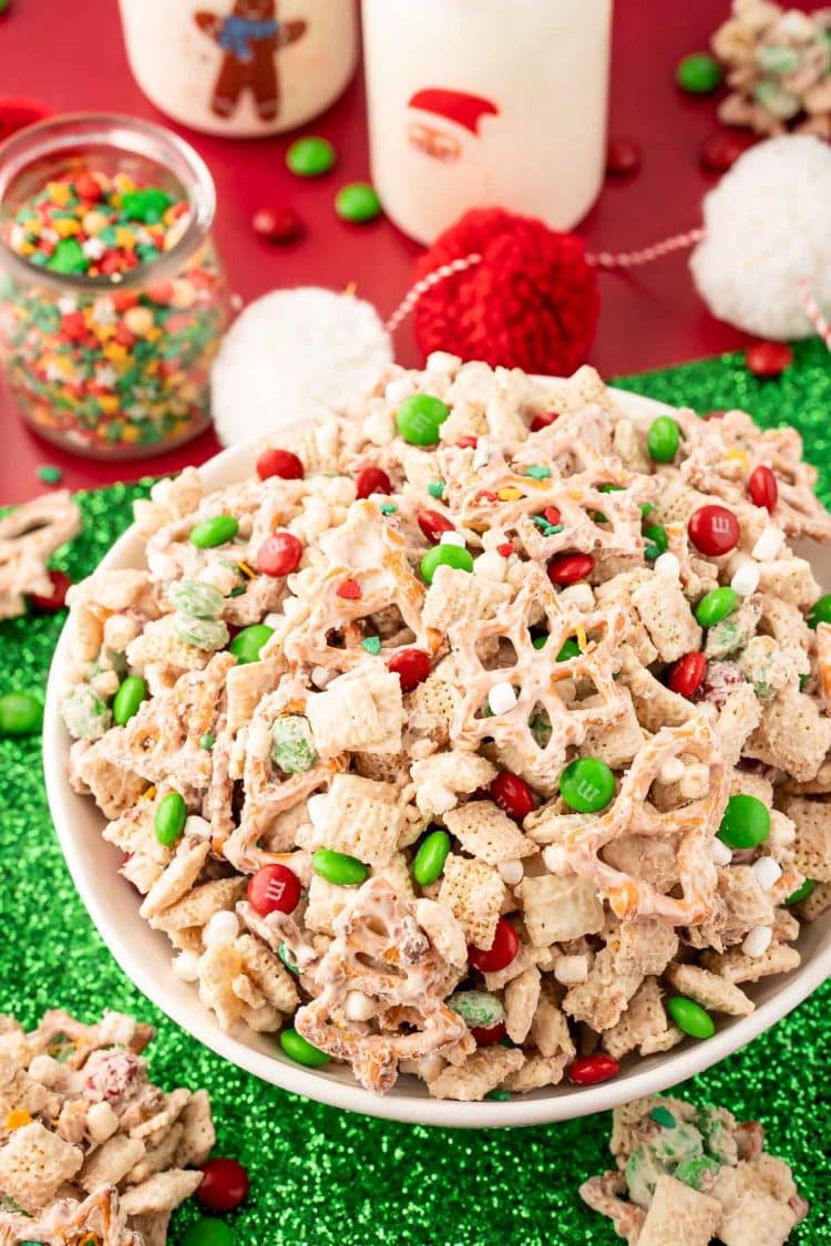 A bowl of Christmas Chex Mix on a green and red holiday decorated table.