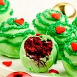 Grinch cake balls on a white plate, the front one if missing a bite to show red velvet inside.