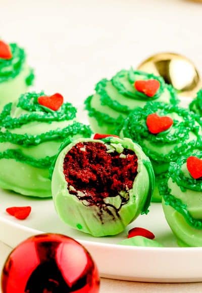 Grinch cake balls on a white plate, the front one if missing a bite to show red velvet inside.