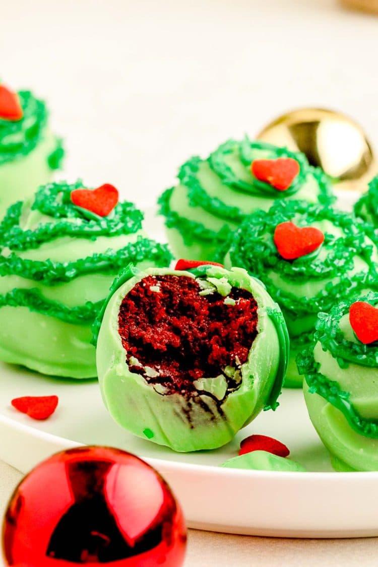 Grinch cake balls on a white plate, the front one if missing a bite to show red velvet inside.