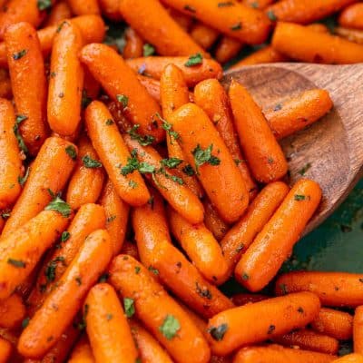 Close up of roasted glazed carrots in a teal baking dish.