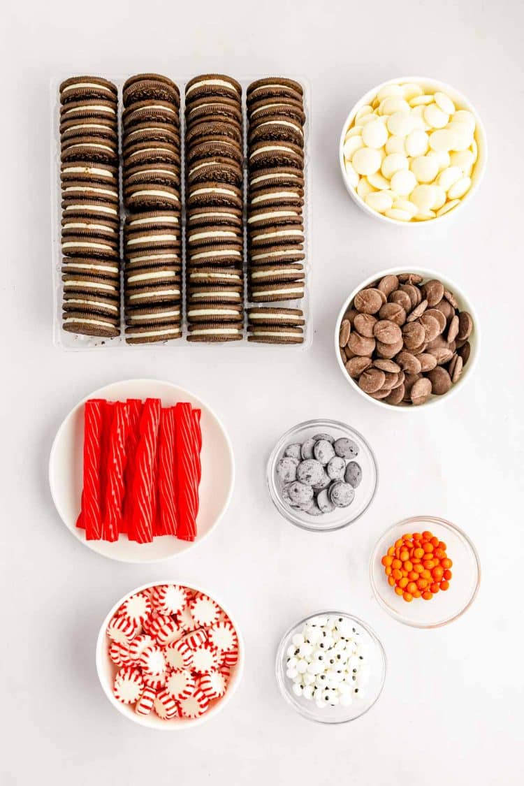 Ingredients to make chocolate covered oreos decorated like penguins on a white surface.