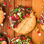 Peanut butter cookies dipped halfway in chocolate and coated with holiday sprinkles on a wooden board.