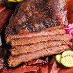 A smoked brisket that's been partially sliced on paper.