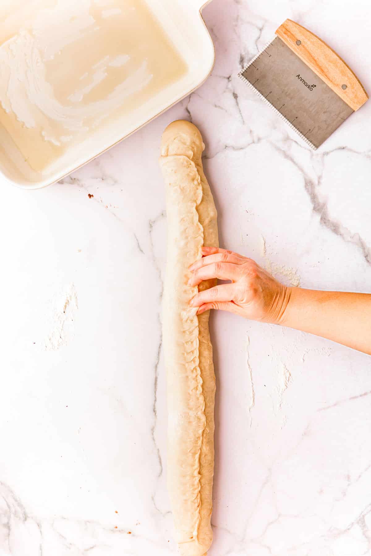 A woman's hand pinch the seams of dough on a log of cinnamon rolls.