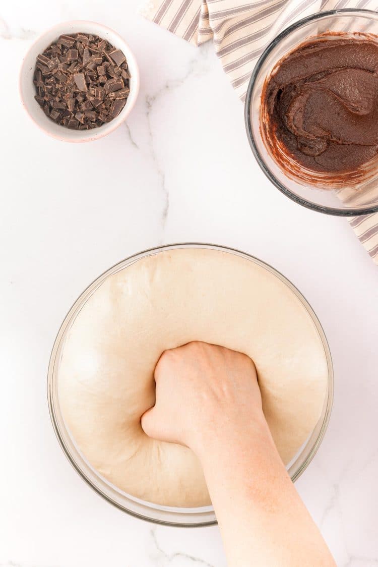 A woman's hand punching down a bowl of dough to make cinnamon rolls.