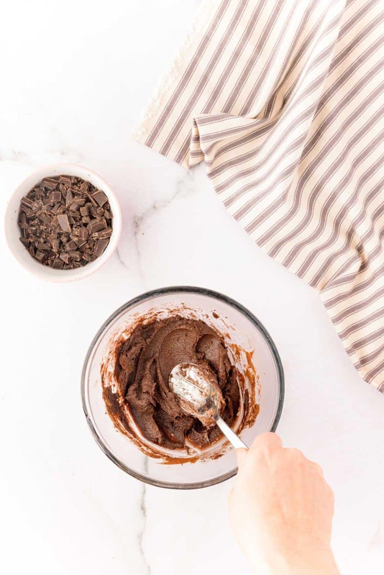 A woman's hand mixing chocolate cinnamon roll filling with a spoon.