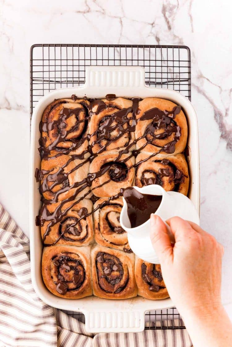 Chocolate glaze being poured over a freshly baking batch of chocolate cinnamon rolls.