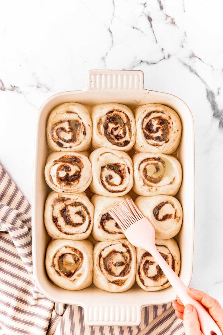 Raised cinnamon rools being brushed with butter before baking.