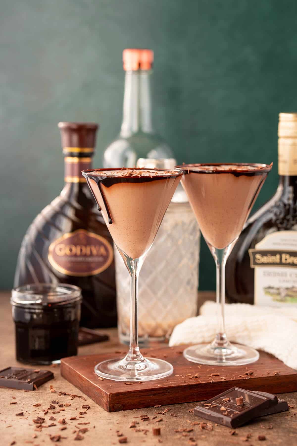 Two martini glasses filled with chocolate martinis on a wooden cutting board.