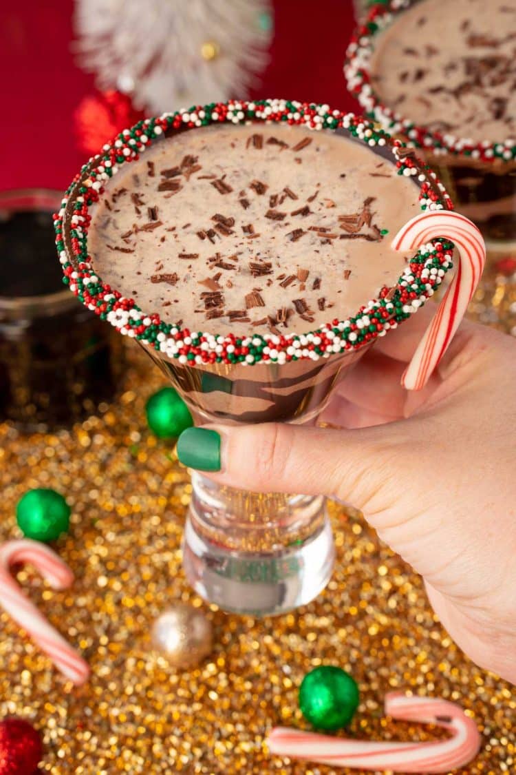 A woman's hand holding a martini glass with a chocolate peppermint martini to the camera.