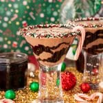 A chocolate peppermint martini on a gold surface with holiday decorations scattered around it.