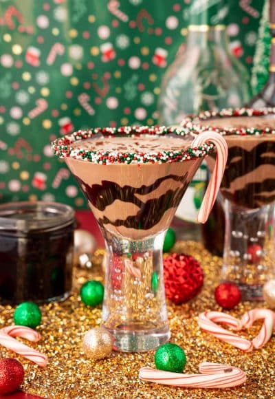 A chocolate peppermint martini on a gold surface with holiday decorations scattered around it.