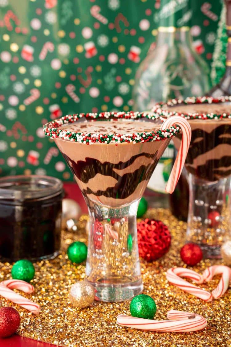 A chocolate peppermint martini on a gold surface with holiday decorations scattered around it.