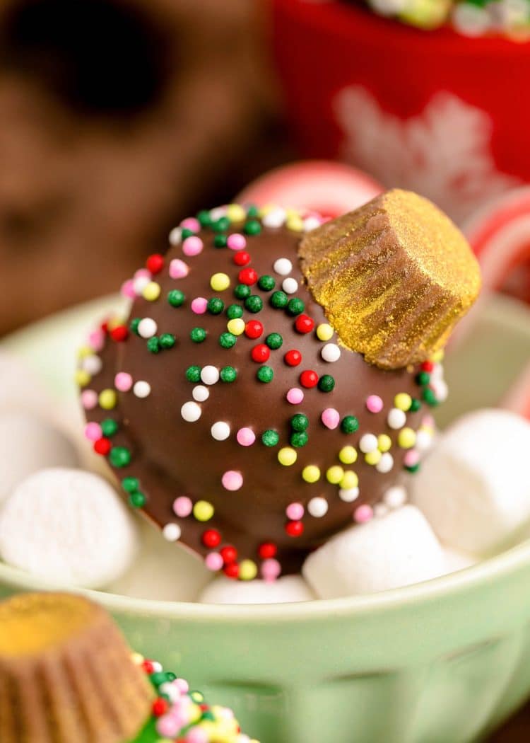 A chocolate covered oreo ball decorated like a Christmas Ornament in a small bowl of marshmallows.
