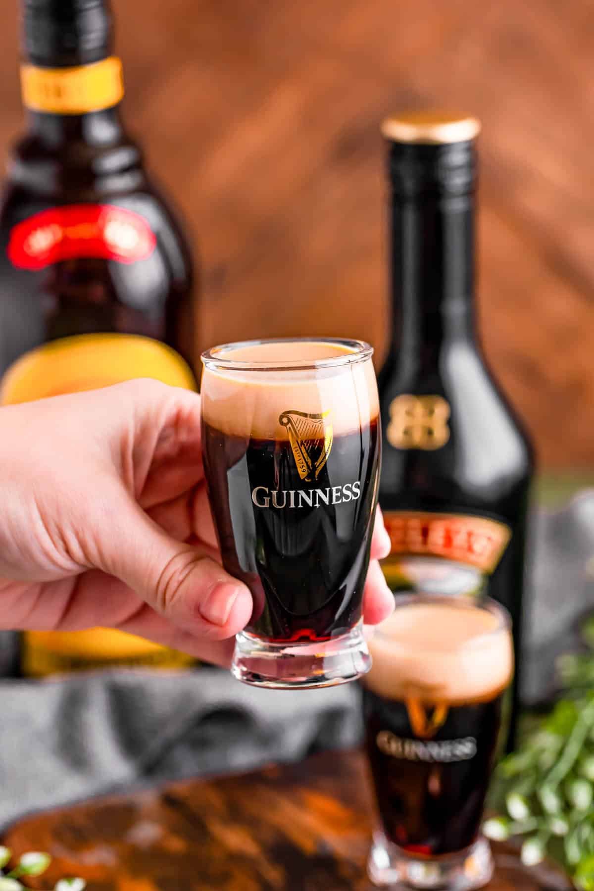 A woman's hand holding a baby Guinness shot to the camera.