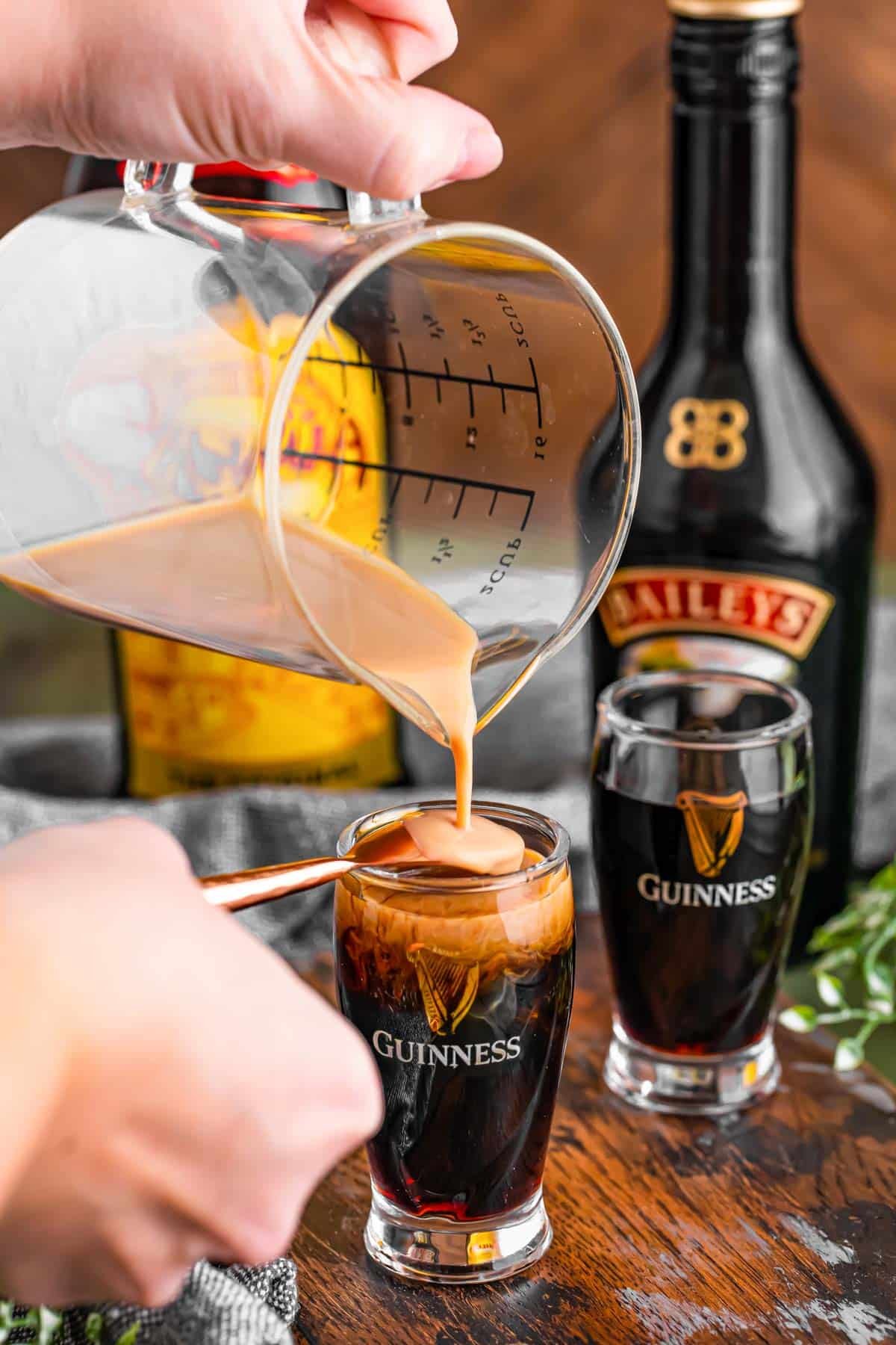 Bailey's Irish cream being poured over the back of a spoon into a shot glass with Kahlua to make a baby Guinness.