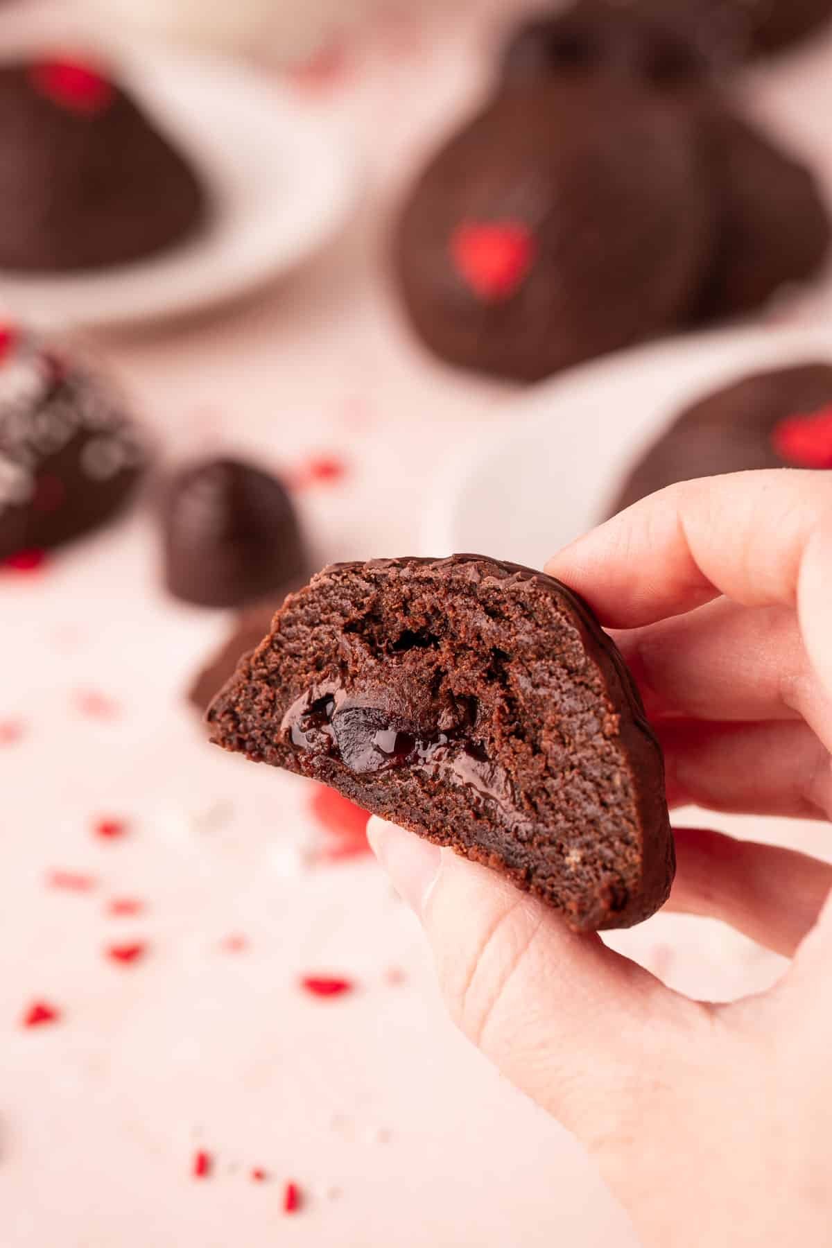 A woman's hand holding a chocolate cookies stuffed with a cherry cordial to the camera.