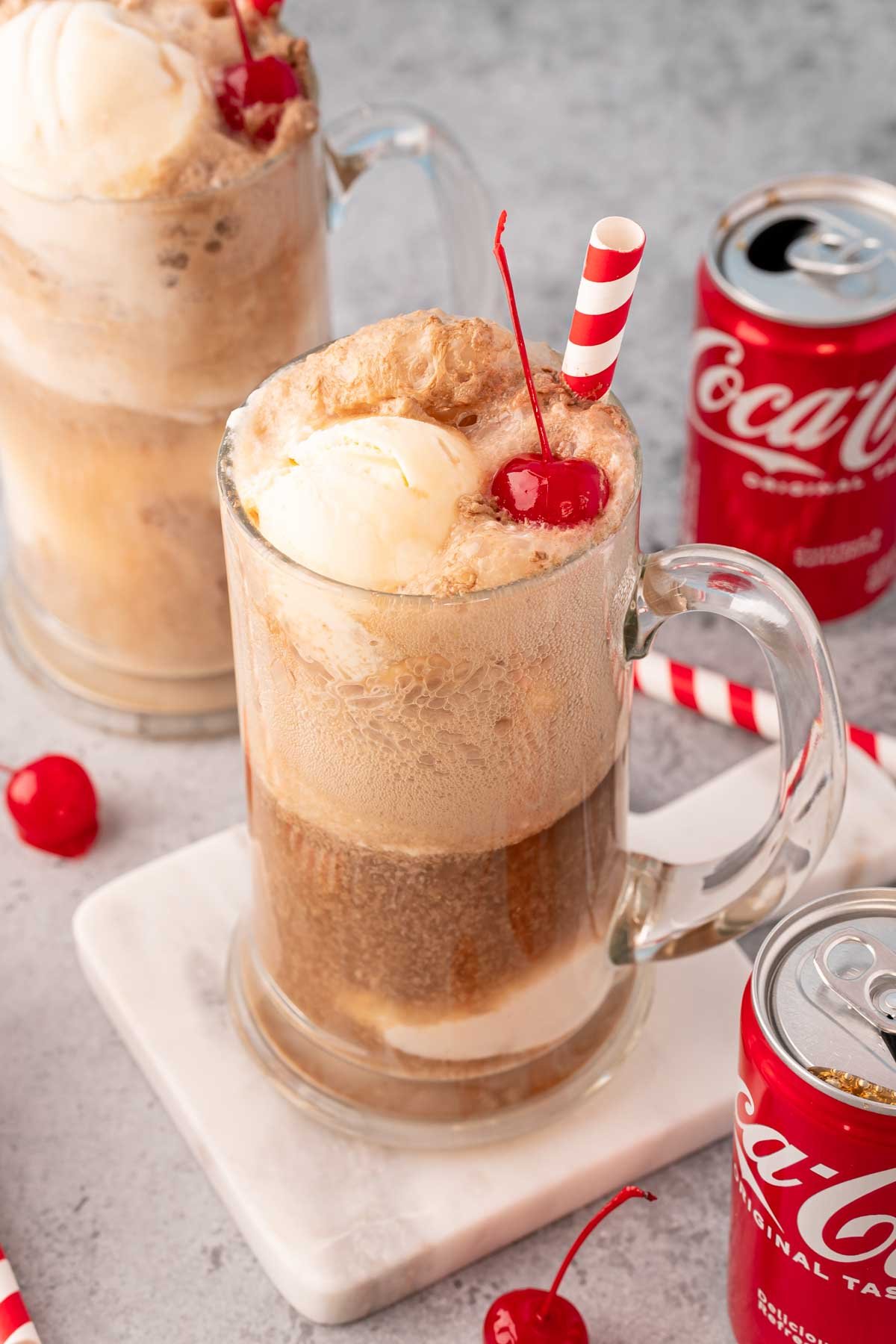 Two beer steins filled with coke floats with coke cans around them.