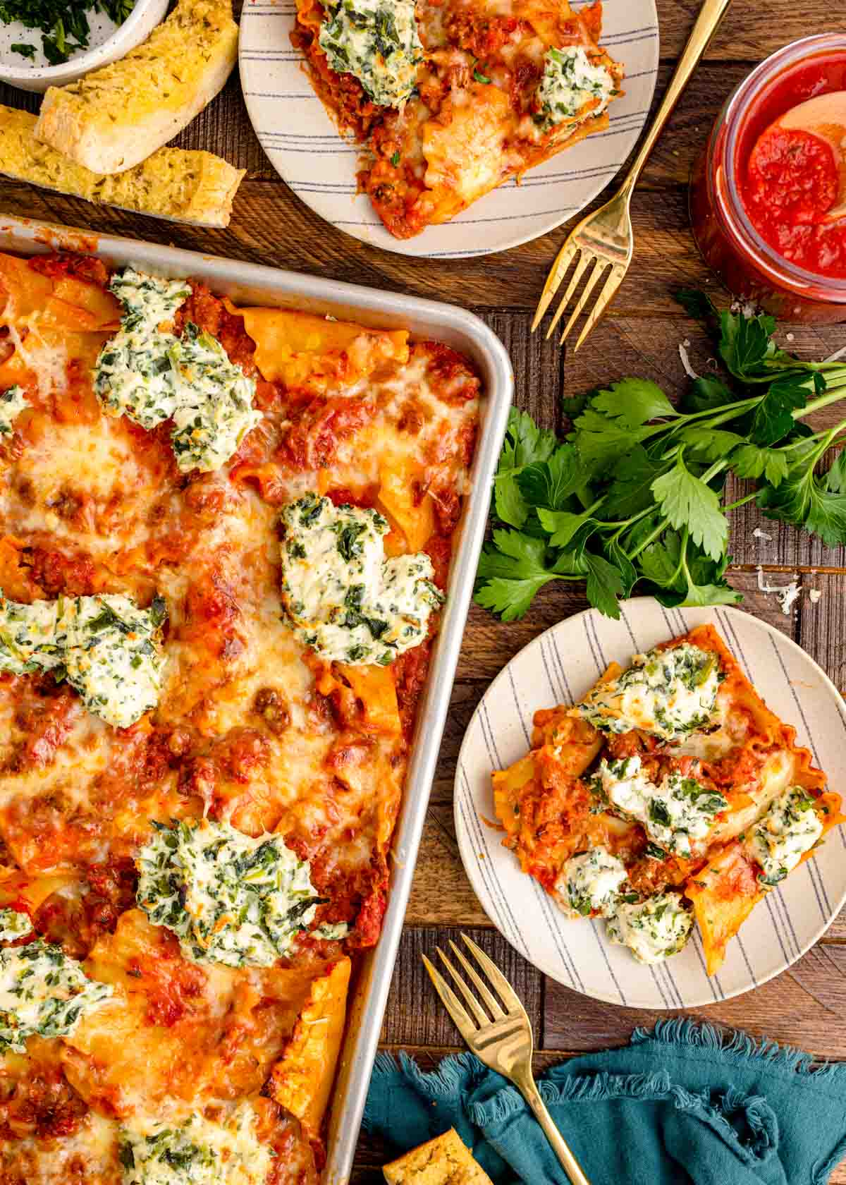 Overhead photo of sheet pan lasagna and slices of it on plates on a wooden table.