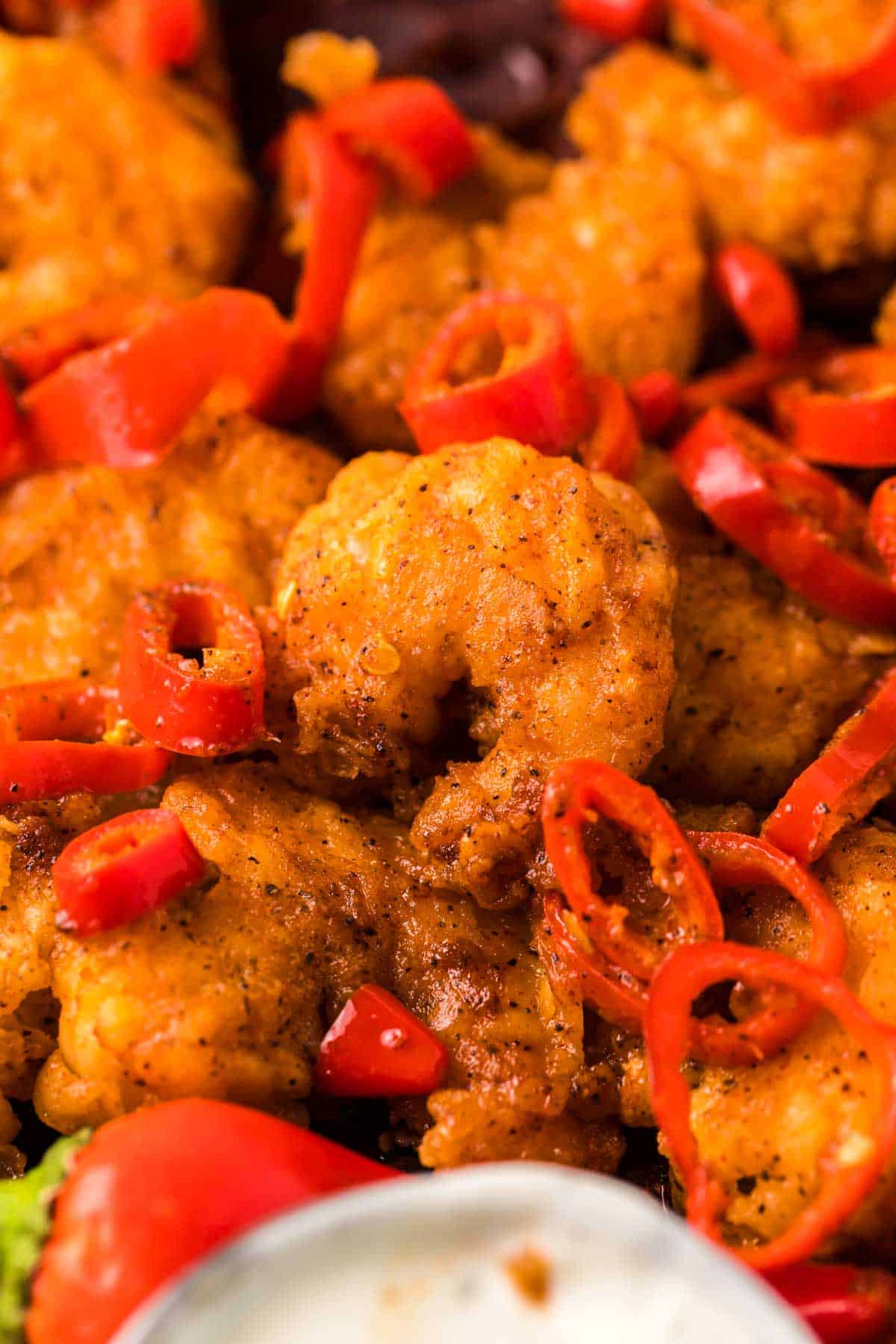 Longhorn copycat wild west shrimp on a plate with red chili peppers and dipping sauce.