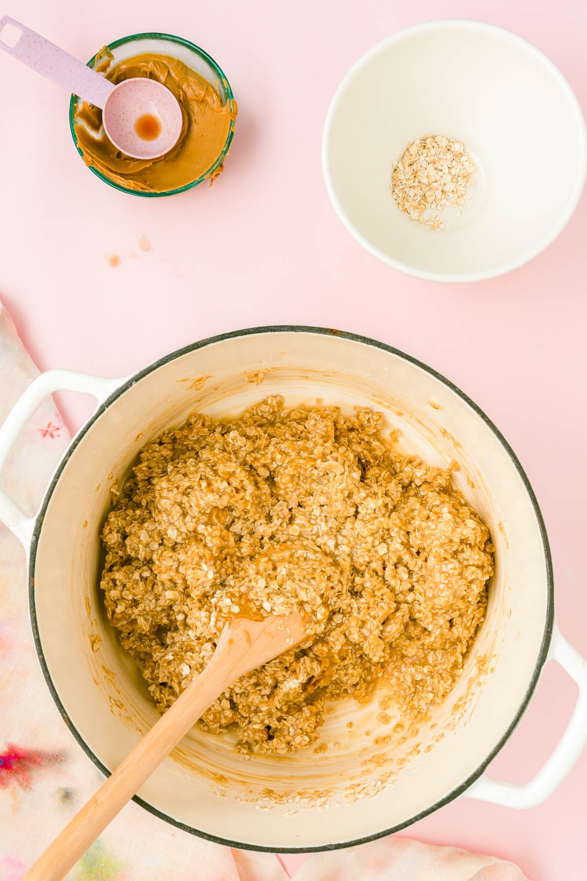 A wooden spoon mixing oatmeal, cookie butter, and vanilla into a pot with butter, milk, and sugar.