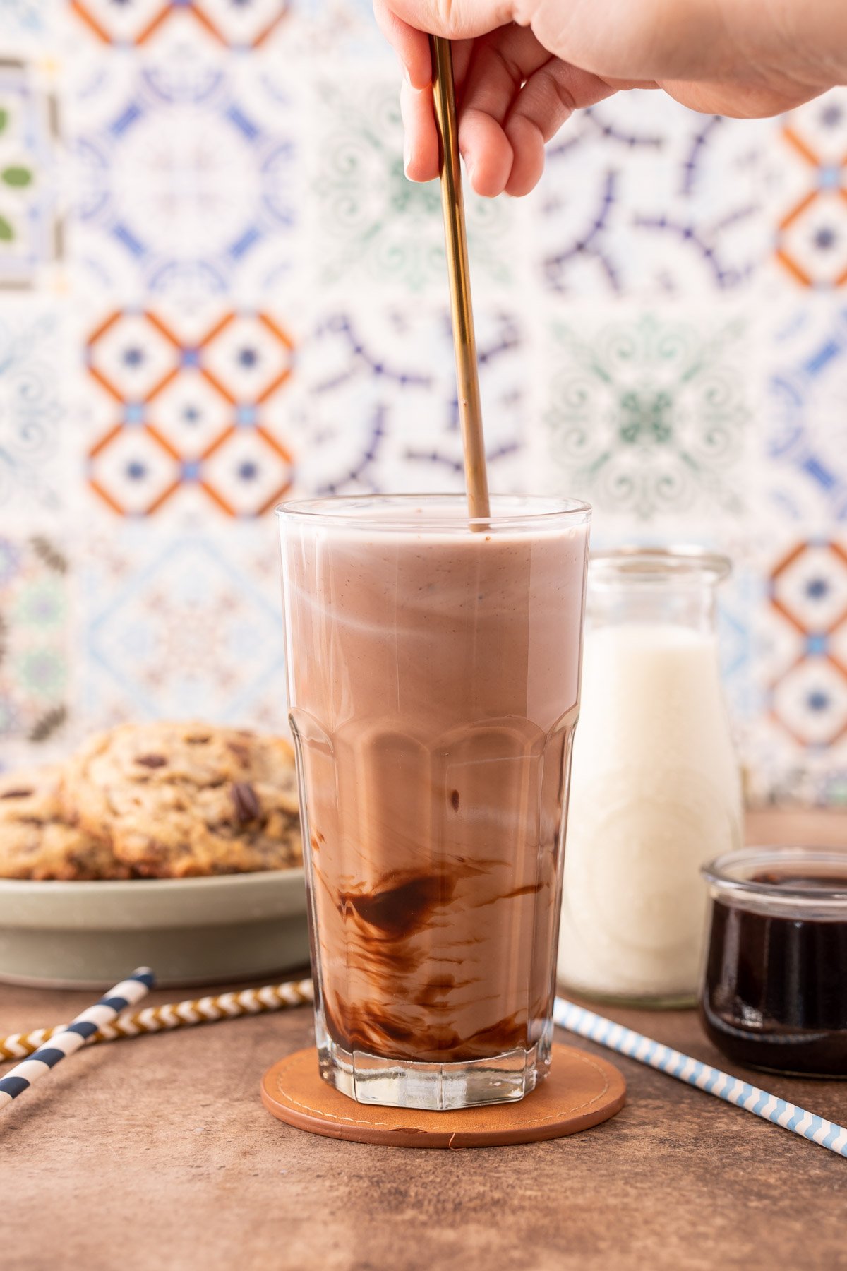 A woman's mixing chocolate milk in a tall glass with a bar spoon.