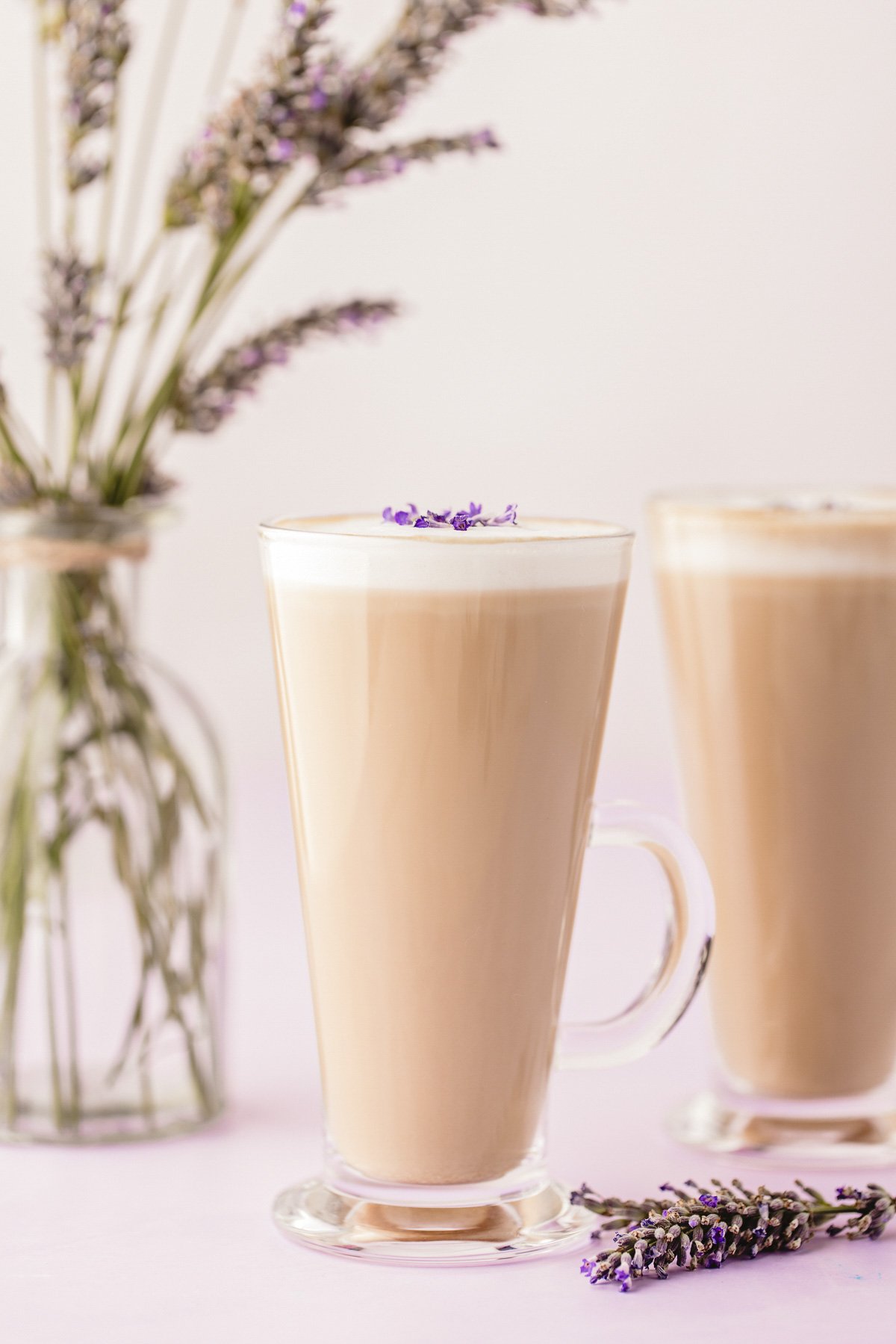 A tapered glass mug with a lavender latte in it, another in the background.