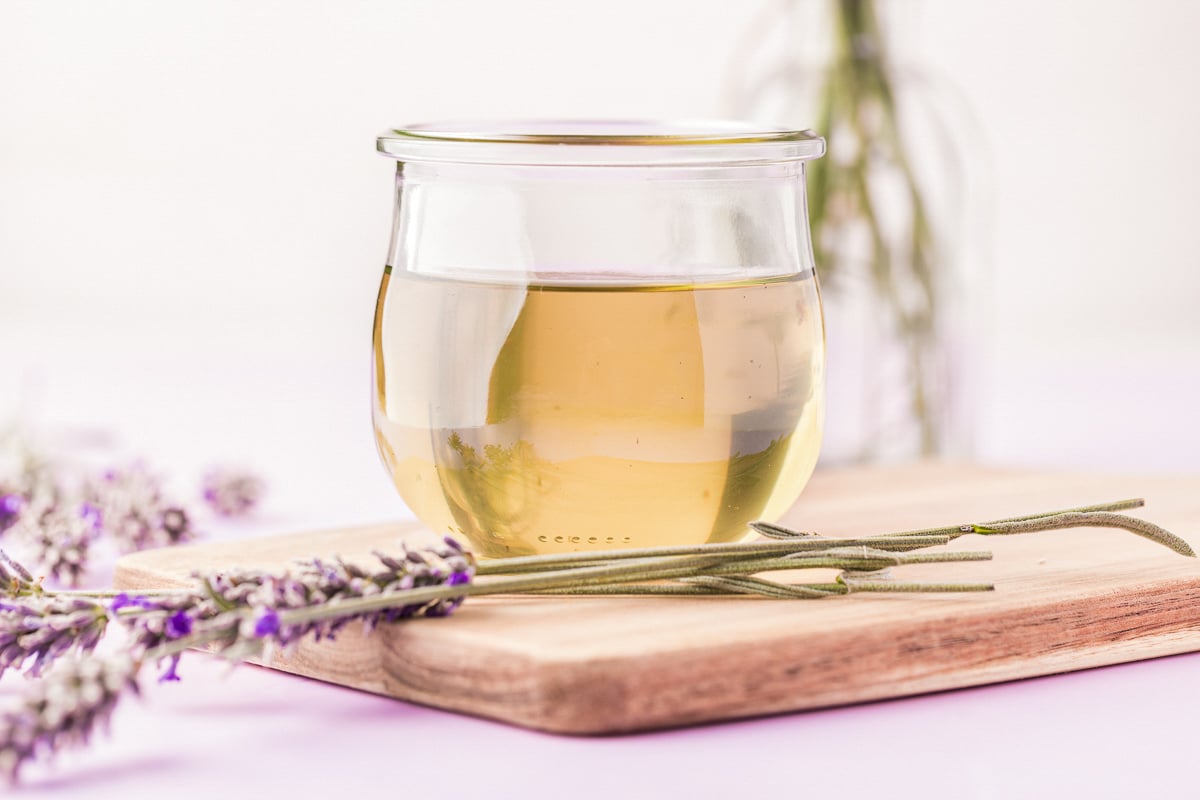 A small jar of lavender simple syrup on a wooden board with lavender around it.