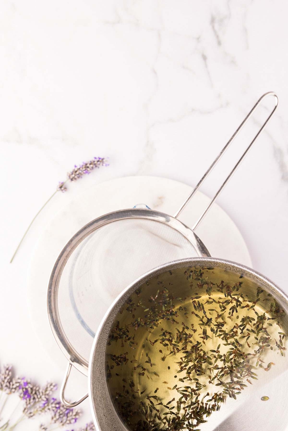 Lavender simple syrup being strained into a measuring cup through a fine-mesh sieve.