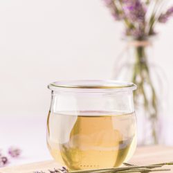 A small jar of lavender simple syrup on a wooden board with lavender around it.