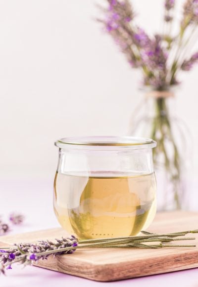 A small jar of lavender simple syrup on a wooden board with lavender around it.