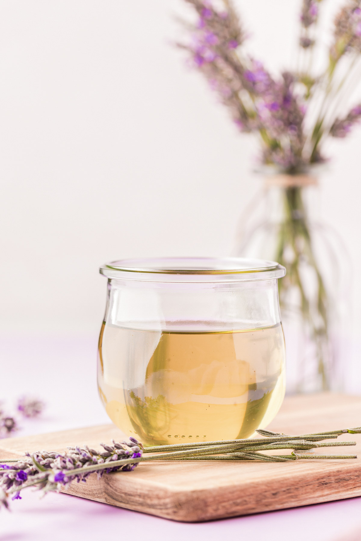 A small jar of lavender simple syrup on a wooden board with lavender around it.