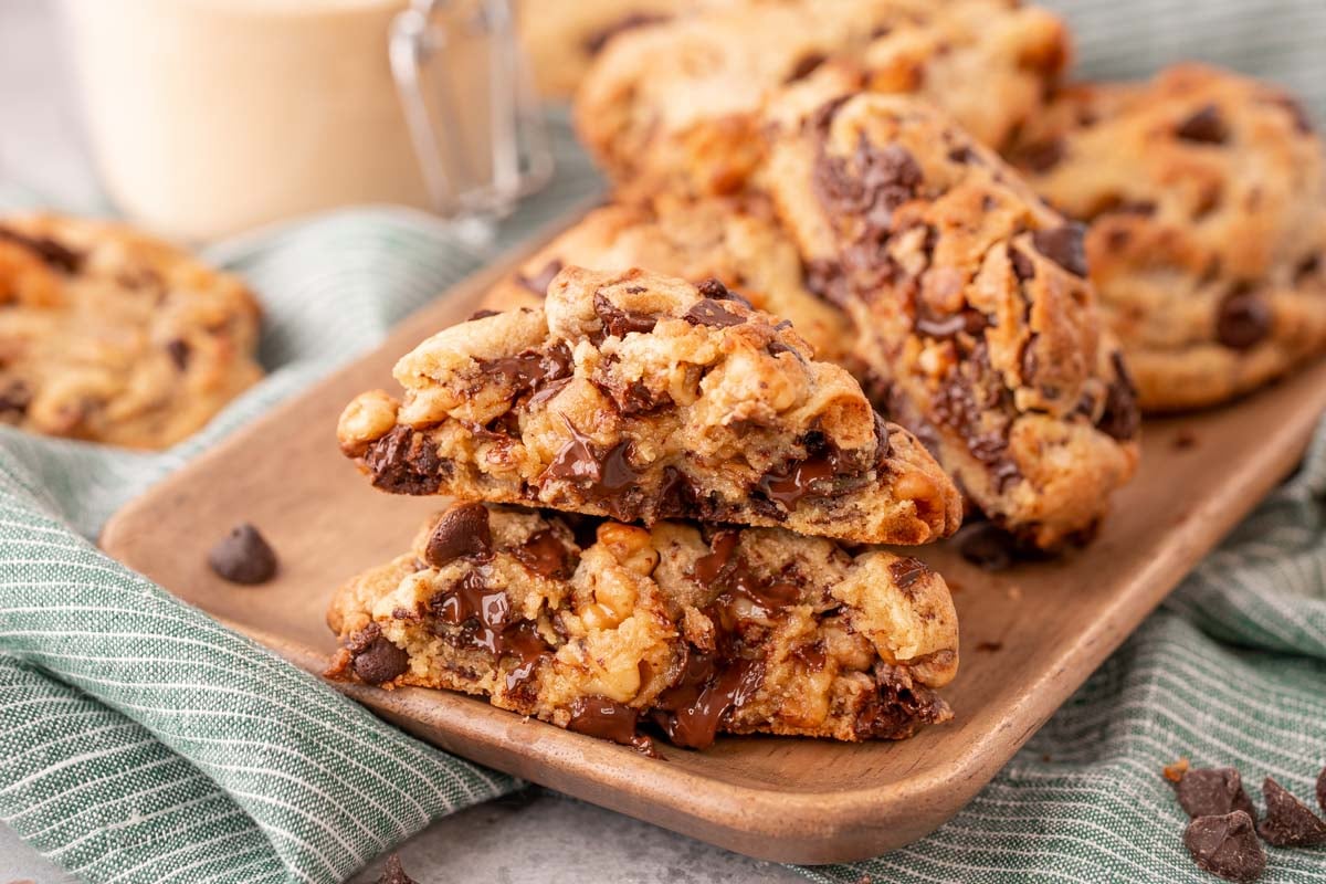 A Levain chocolate chip cookie has been broken in half and the halves are stacked on top of each other on a wooden plate.