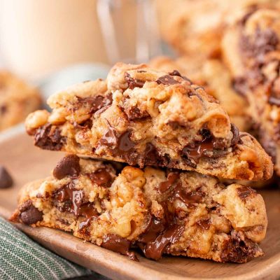 A Levain chocolate chip cookie has been broken in half and the halves are stacked on top of each other on a wooden plate.