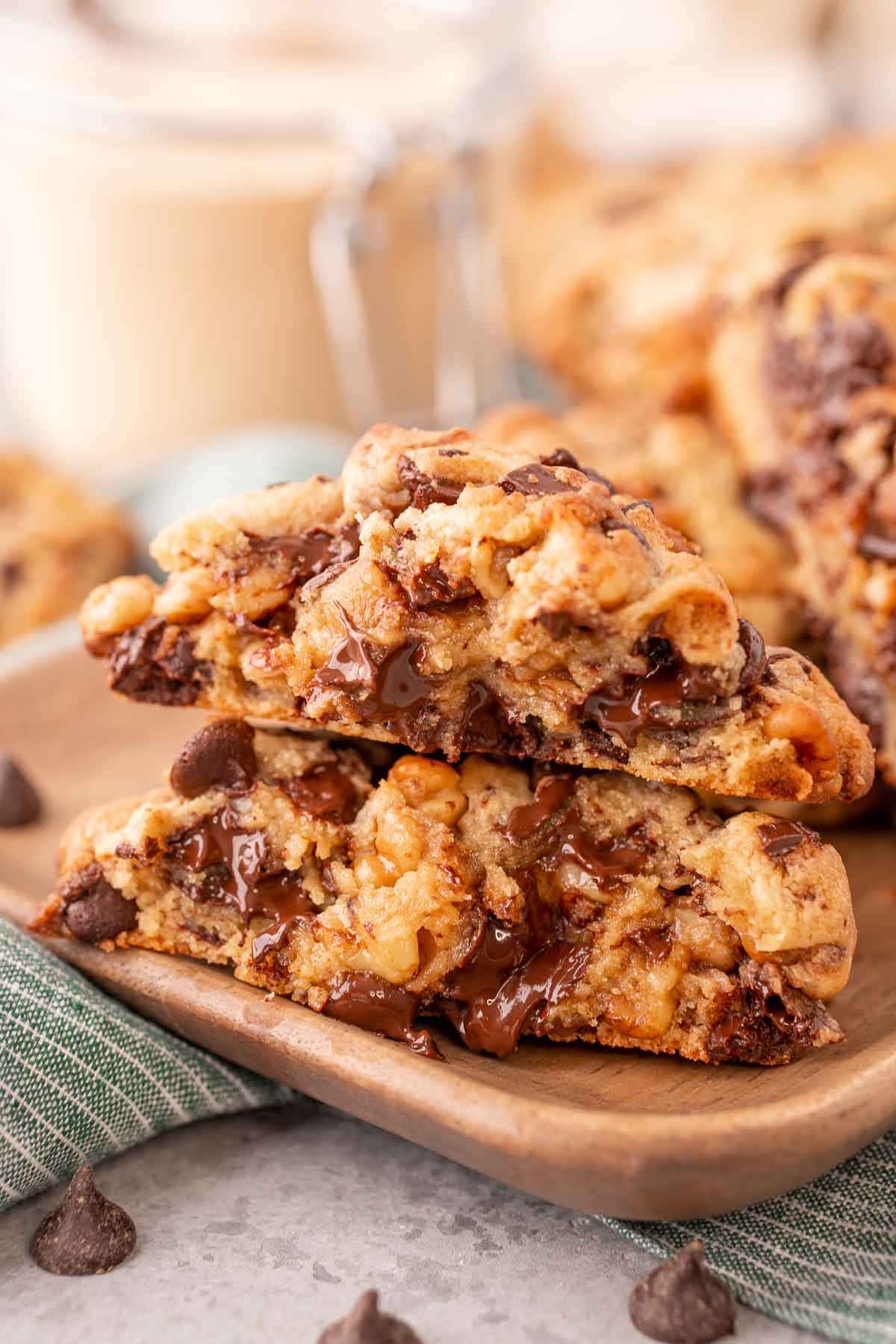 A Levain chocolate chip cookie has been broken in half and the halves are stacked on top of each other on a wooden plate.