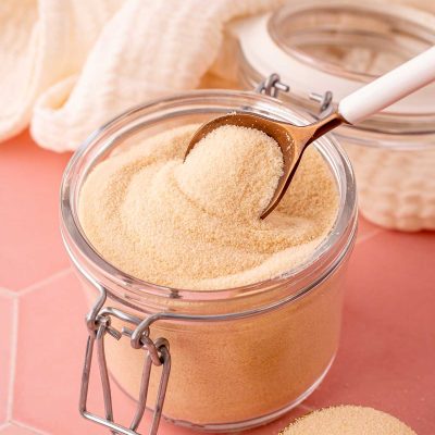 A spoon scooping toasted sugar out of a glass canister.