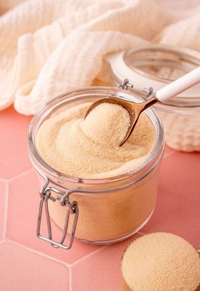 A spoon scooping toasted sugar out of a glass canister.