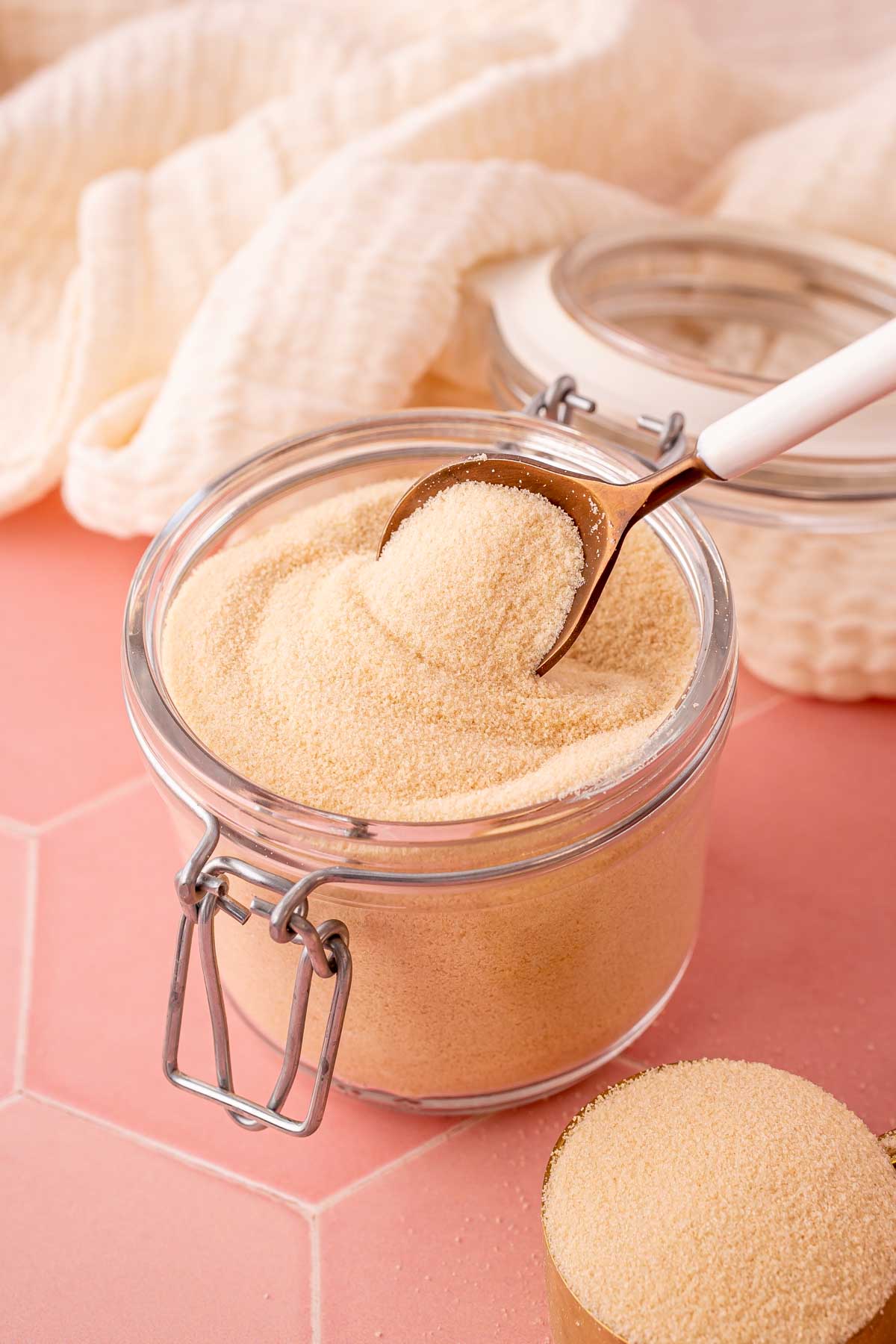 A spoon scooping toasted sugar out of a glass canister.