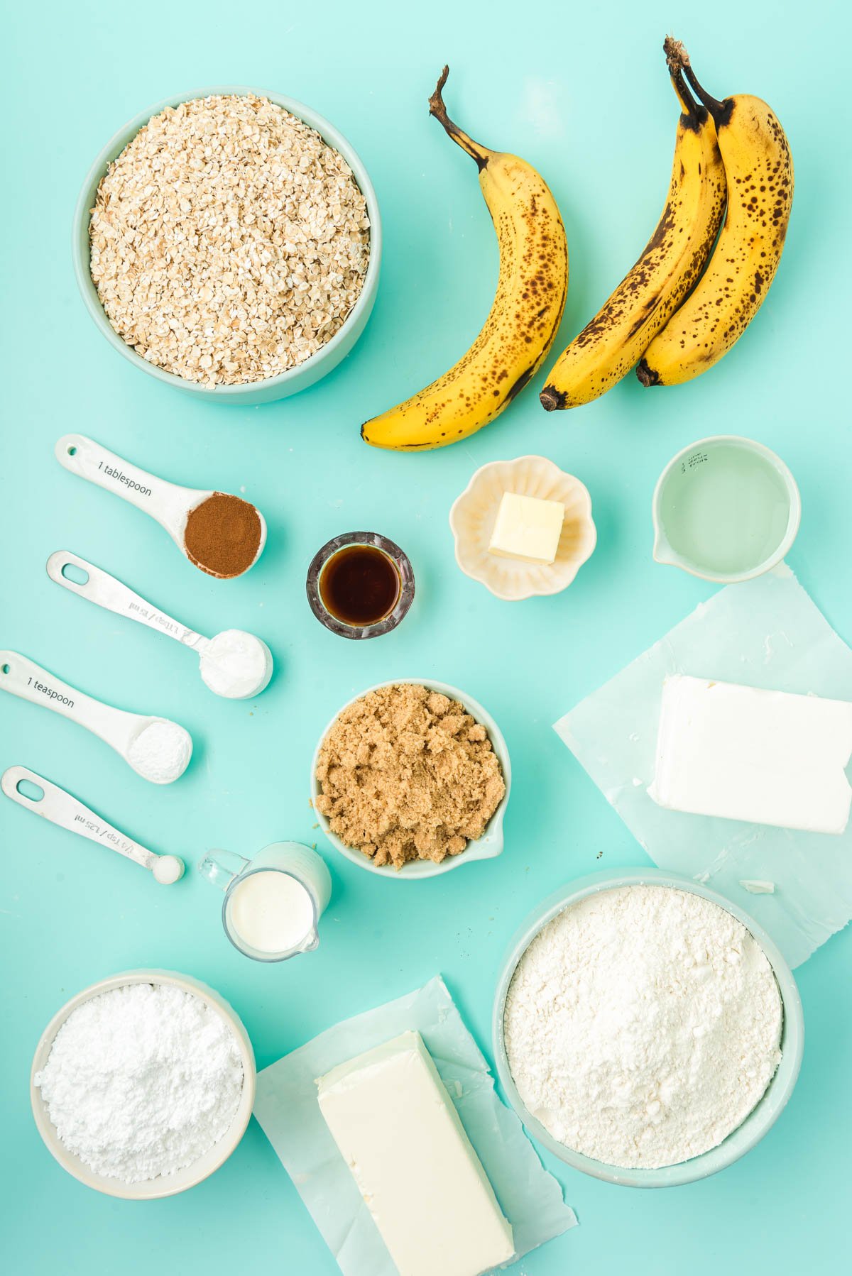 Overhead of ingredients prepped to make banana oatmeal cream pies on a blue surface.