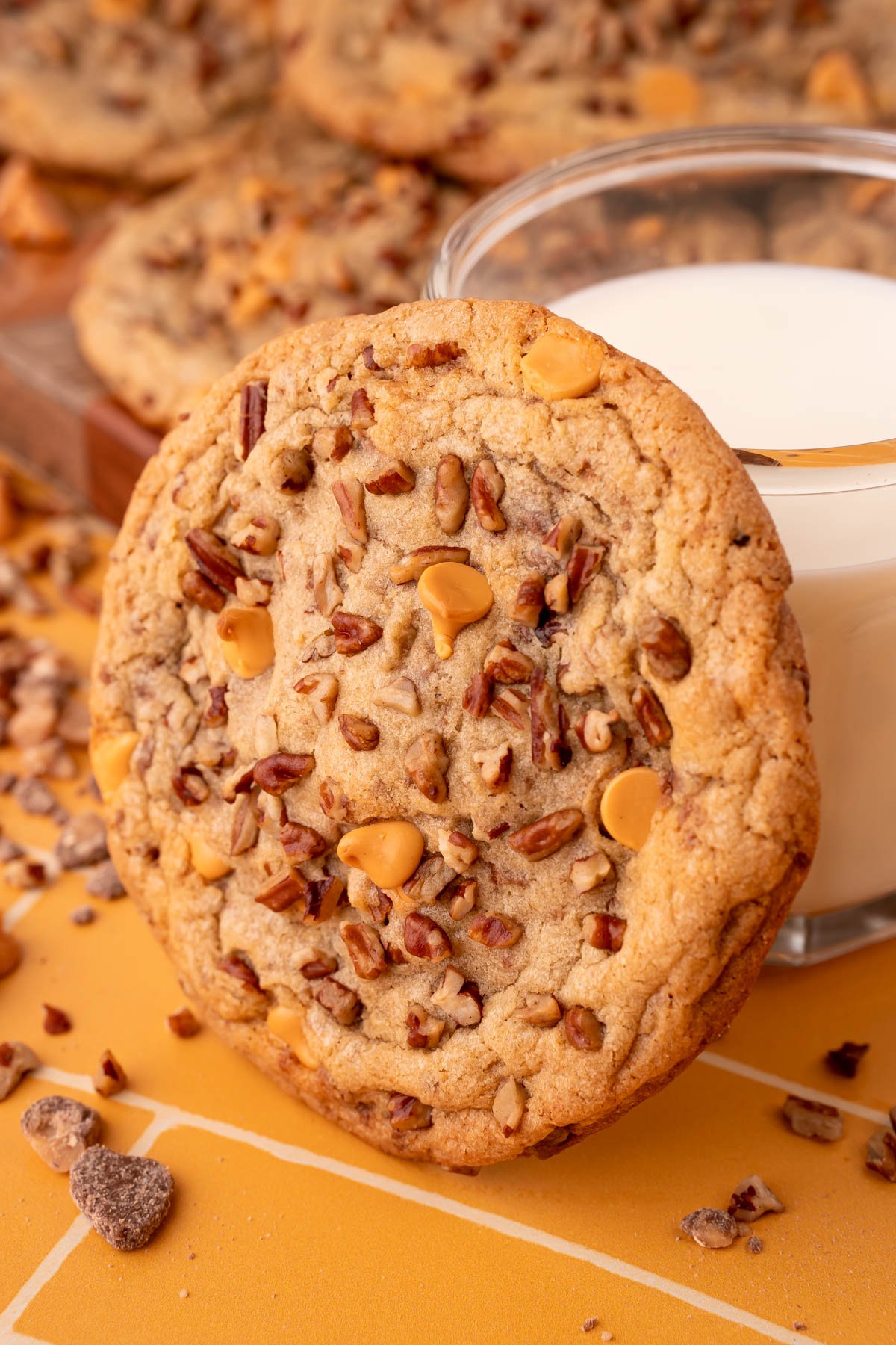 A large butter pecan cookie leaning against a glass of milk.