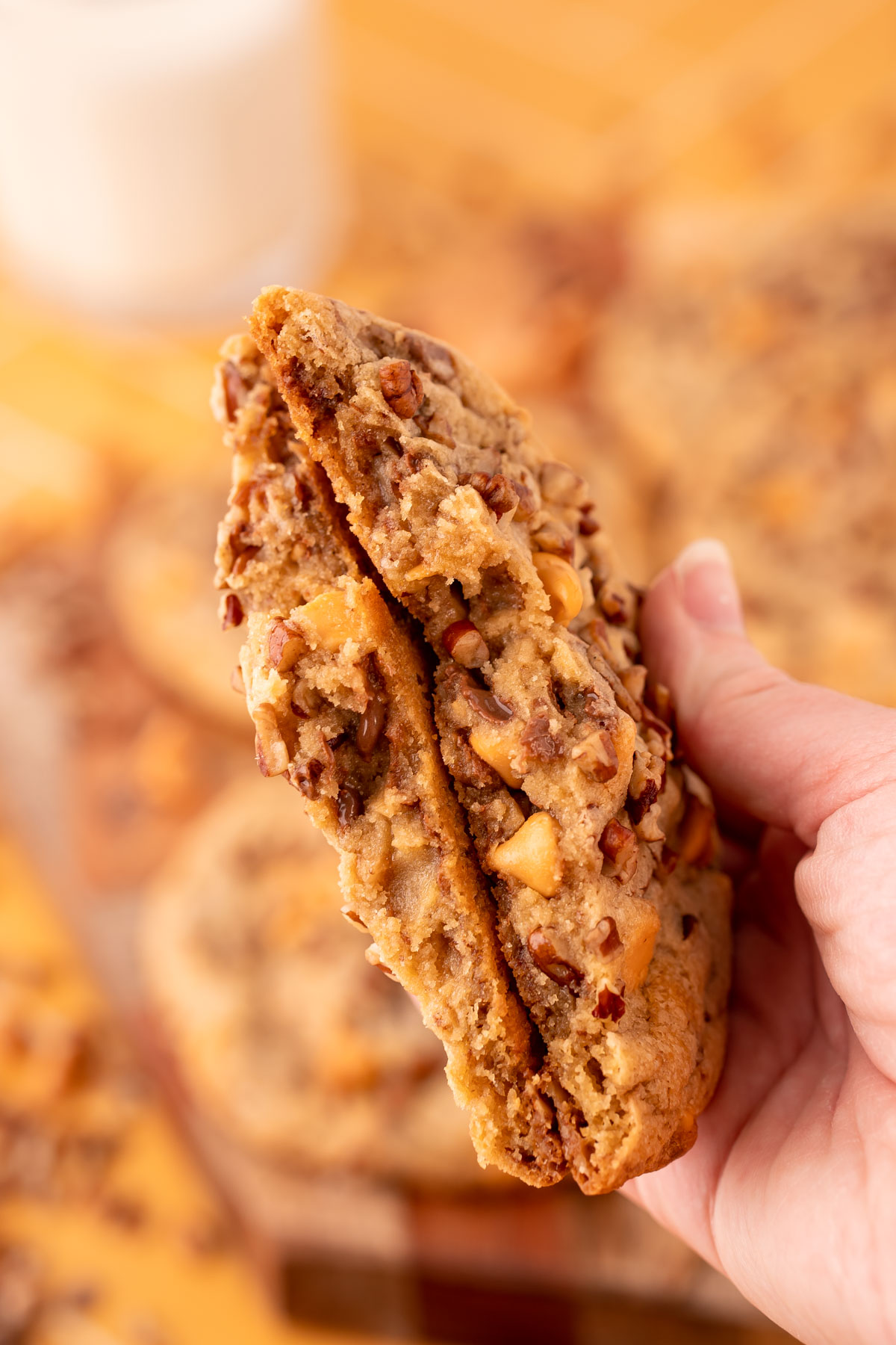 A large butter pecan cookie that has been broken in half in a woman's hand to show the texture of the center.