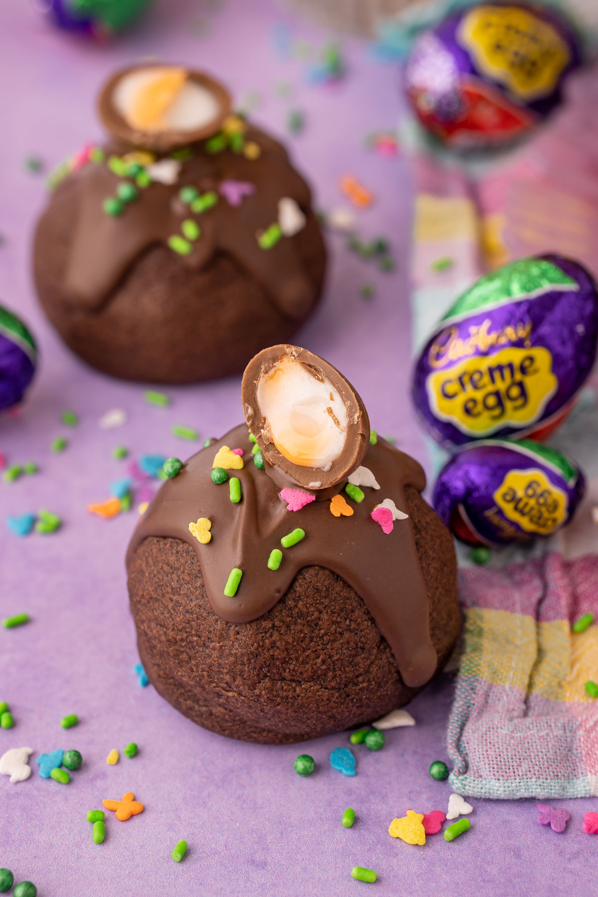 A chocolate cookie topped with mini cadbury creme egg on a purple surface.