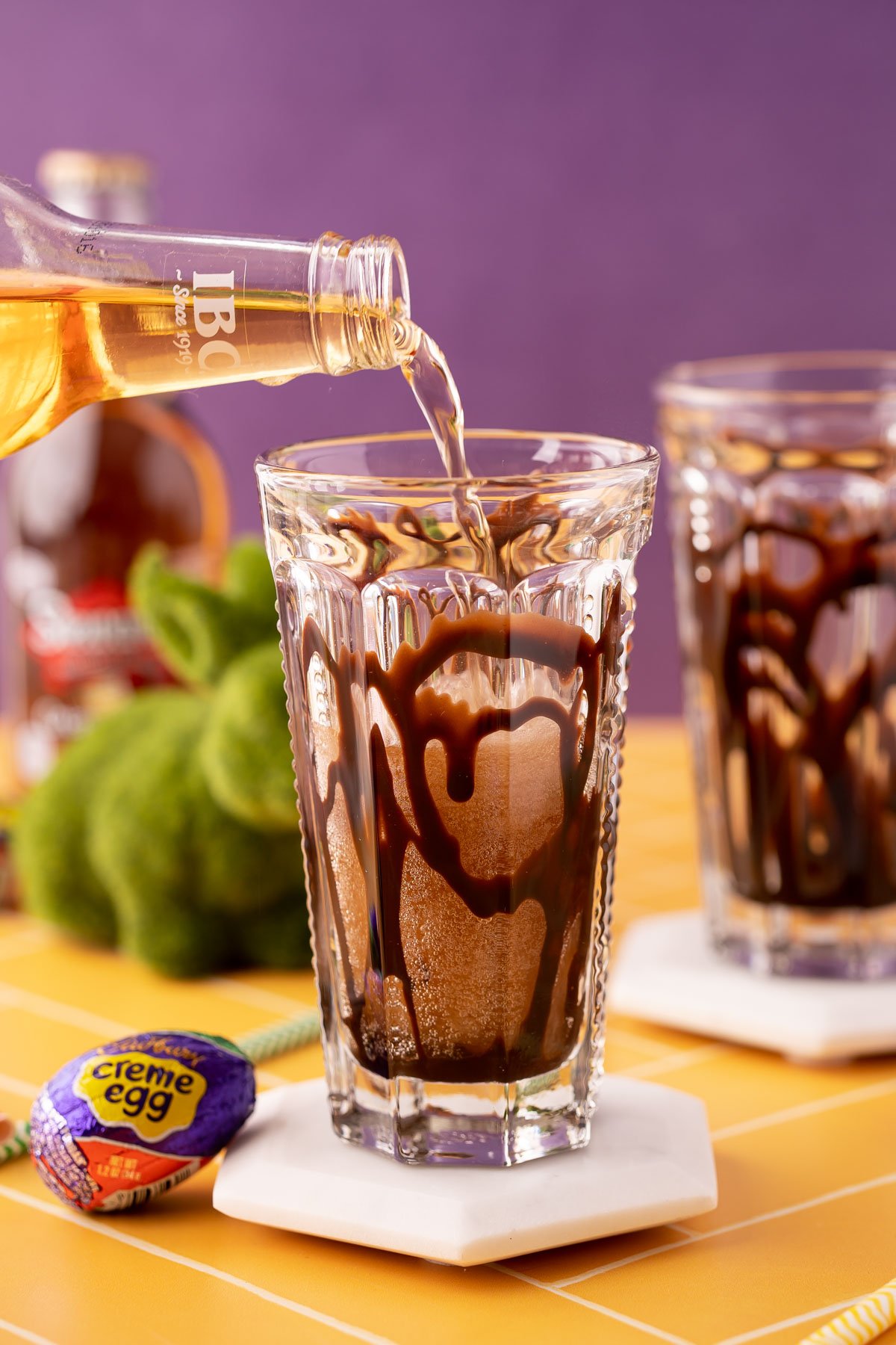 Cream soda being poured into a glass with chocolate syrup.