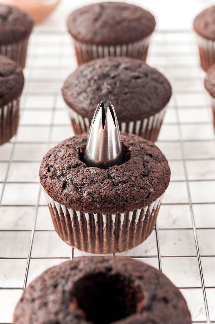 A piping tip coring the center out of a chocolate cupcake.