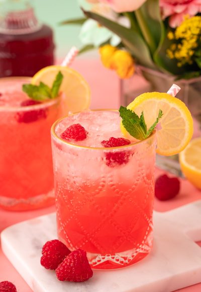 Close up of a raspberry gin daisy on a white marble coasted on a pink table.